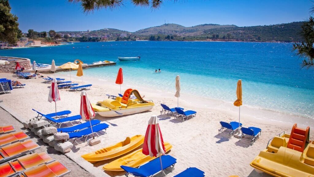 Family-friendly beach with colorful pedal boats, sun loungers, and umbrellas along a calm turquoise bay in Albania"