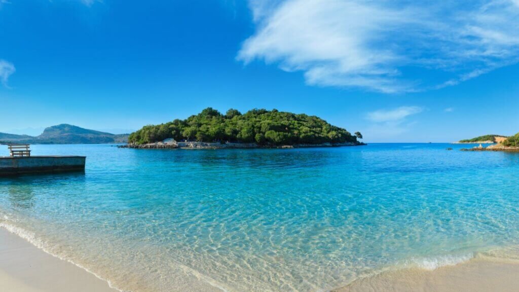 Crystal-clear turquoise lagoon with a sandy beach, sun loungers, and small islands near Ksamil, Albania