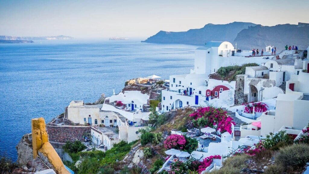 Blue dome churches and whitewashed village buildings in Oia, Santorini, captured during a bright golden sunset over the Aegean Sea.