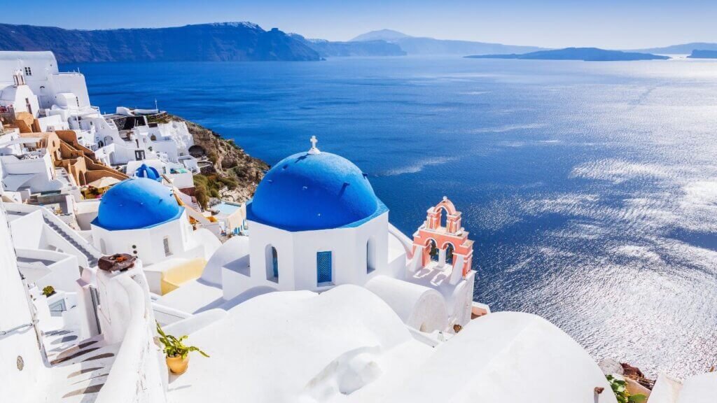 Panoramic view of whitewashed cliffside houses, yellow cave homes, and traditional windmills in Oia, Santorini.