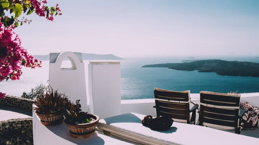Sun loungers on a whitewashed resort patio overlooking the volcanic caldera and ocean in Santorini on a sunny day.